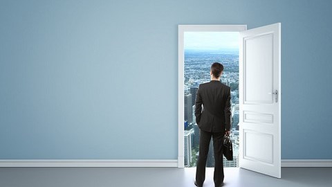 In empty blue room of a house a businessman with briefcase stands in front of an open door with a long-range view of a city