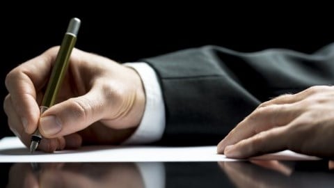 A businessman's hand holding a pen and writing a letter