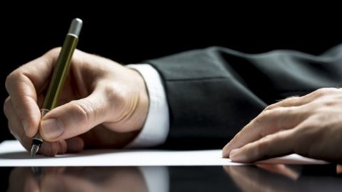 A businessman's hand holding a pen and writing a letter