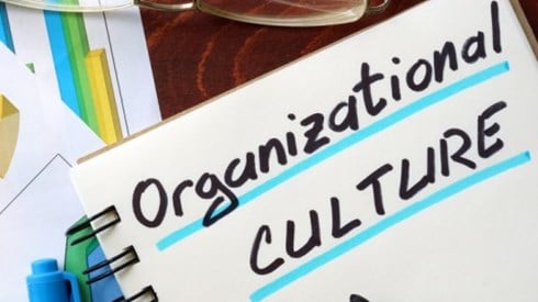 A desk has printouts of statistics, eyeglasses, a marker, and a note pad with the words Organizational Culture underlined