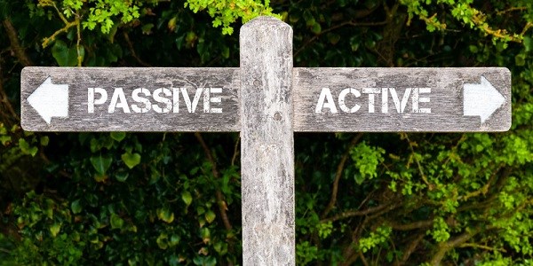 A wooden crossroads sign with the word PASSIVE with an arrow pointing left and the word ACTIVE with an arrow pointing right