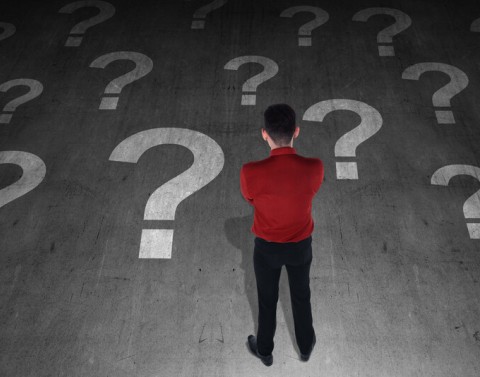 A man is standing and thinking while looking at a floor painted with large question marks