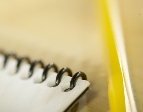 The corner of a black spiral bound notebook on an indistinct yellows background