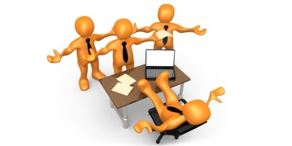 Three standing businessmen icons are upset with one in chair with legs on top of desk that has a laptop and papers on it