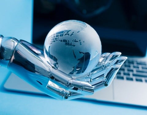 Robot hand holding globe in palm with computer screen in background
