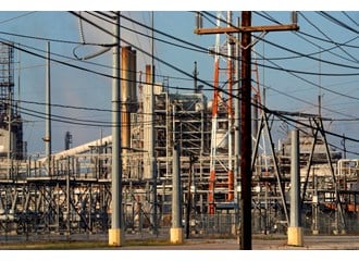 A power transfer station for an electrical plant and industrial type buildings behind with blue sky in background