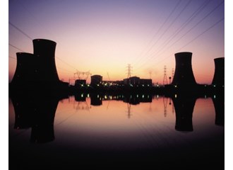 Nuclear power plant located on waterfront with evaporation silos and plant reflecting in water at sunset