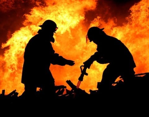 Two firefighters work to extinguish a raging fire