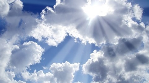Bright sun rays bursting through a cloud in a partly cloudy blue sky