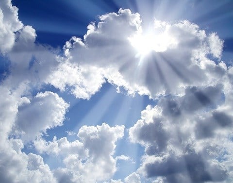 Bright sun rays bursting through a cloud in a partly cloudy blue sky