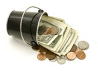 A small black bucket laying on its side with coins and dollar bills spilling out of it 