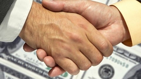 Two businessmen shaking hands over a background of one hundred dollar bills