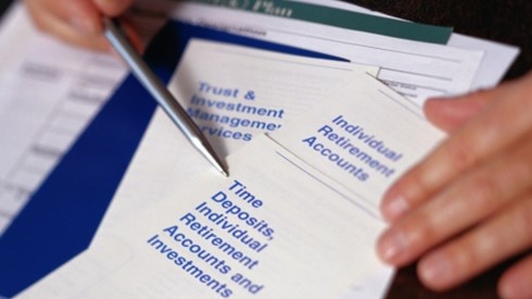 Two hands with a pen pointing to an Individual Retirement Account pamphlet with plan forms beneath it