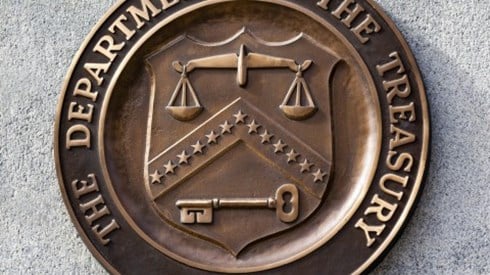 Metal sign mounted on a concrete block building showing THE DEPARTMENT OF THE TREASURY 1789 seal 