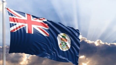 The flag of the Cayman Islands flying in a sunbeamed sky
