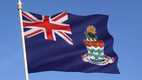 Cayman flag flying on a pole with a blue sky background