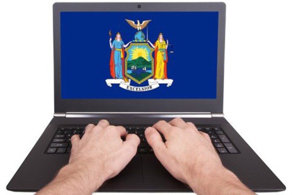 Male hands typing on laptop with blue background and New York seal