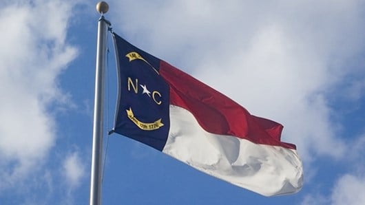 Flag of the State of North Carolina Flying on Flagpole Against Blue Sky with Clouds
