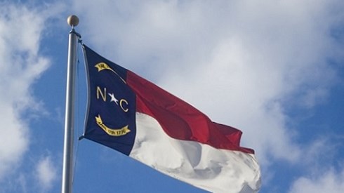 The North Carolina flag on a flag poll waving in front of a blue sky with clouds