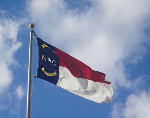 The North Carolina flag on a flag poll waving in front of a blue sky with clouds