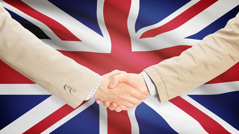 Two business people in suits shaking hands in front of a background of the UK flag