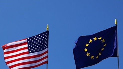 United States and European Union flags flying on poles with blue sky background