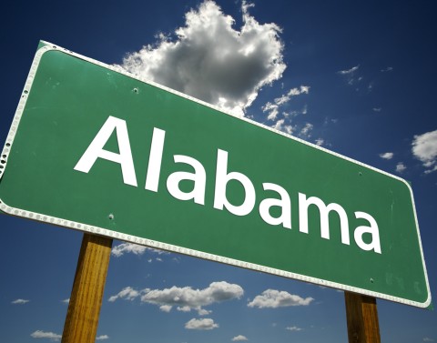 Green road sign with Alabama written on it and a blue sky with clouds in the background.