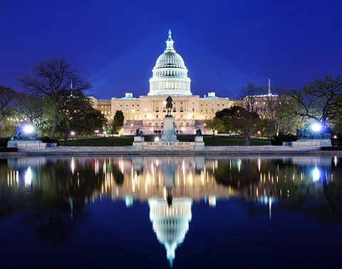 Night view of Capitol Building with reflection showing in water in front of it and spotlights shining on it