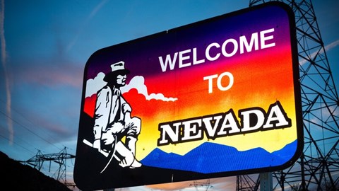 A sign saying WELCOME TO NEVADA with an old male gold miner kneeling with his pickaxe and gazing at the mountain sunset