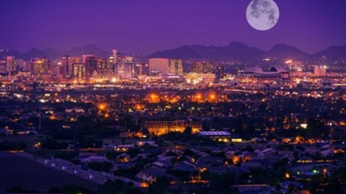 Nighttime city overview of Phoenix, Arizona, with mountains and large full moon in background