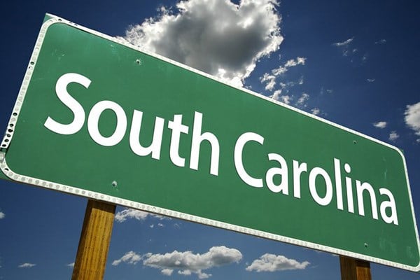 Road sign reading South Carolina against a blue sky with clouds