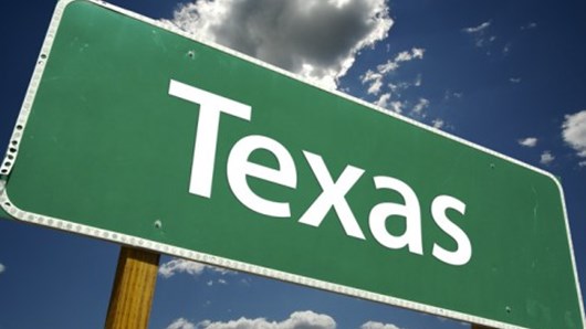 Green road sign of Texas in front of blue sky with clouds