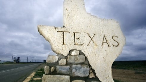 A pile of rocks mounded on the side of a road with the top rock in the shape of and word Texas in the middle welcoming incoming visitors.