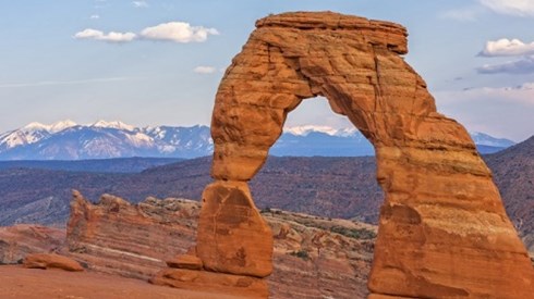 Orange colored sandstone arches in the Utah Arches National Park with mountains and blue sky in the background