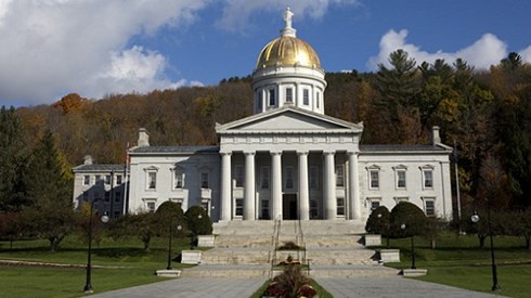 Promenade and stairs leading up to white Vermont State House with columns and gold dome with trees and blue sky behind