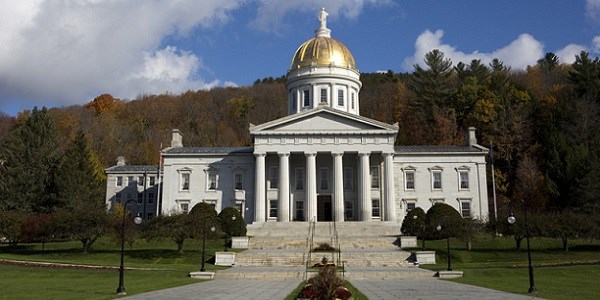 Promenade and stairs leading up to white Vermont State House with columns and gold dome with trees and blue sky behind
