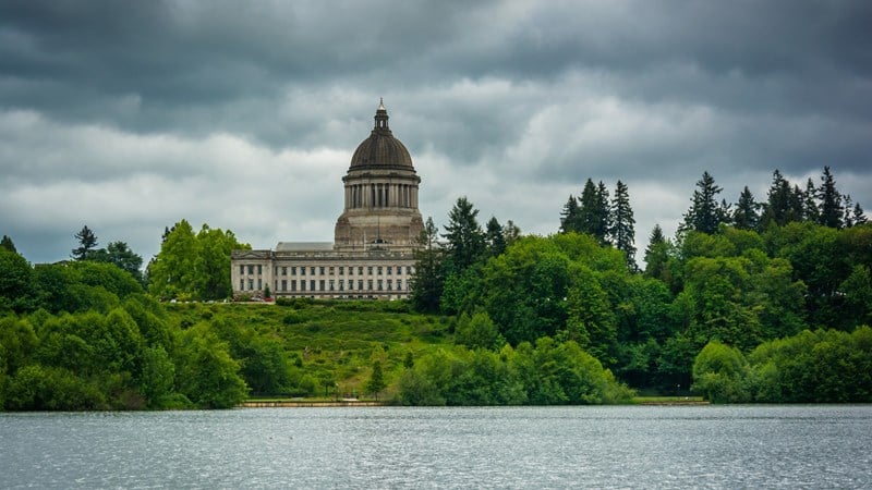 Washington State capitol building against cloudy sky surrounded by trees by Capitol Lake 
