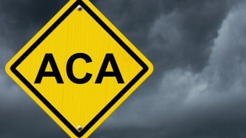 Yellow diamond warning traffic sign that says ACA with a dark cloudy sky in the background