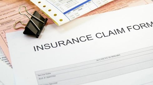 Insurance claim forms on white, yellow, and pink paper with binder black clip