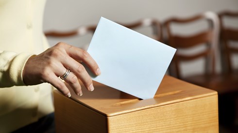 Woman putting folded vote into wooden ballot box
