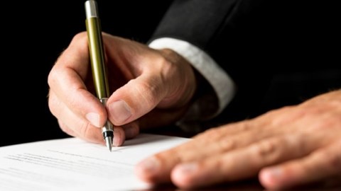 A businessman is using one hand to support a document and the other to sign it.