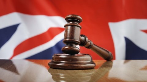 A gavel lying on its base on a desk with the Union Flag of the United Kingdom in the background