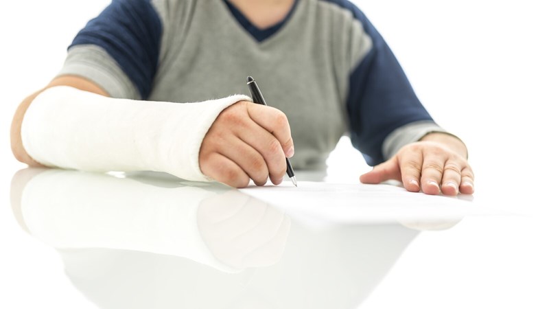 Person with cast covering hand and arm up to elbow writes on paper with a pen