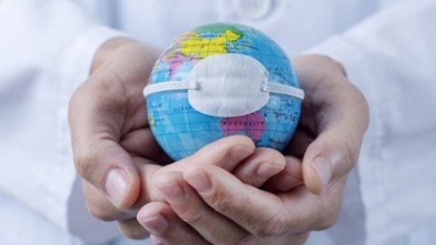 Cupped hands holding a small globe with a medical mask on it