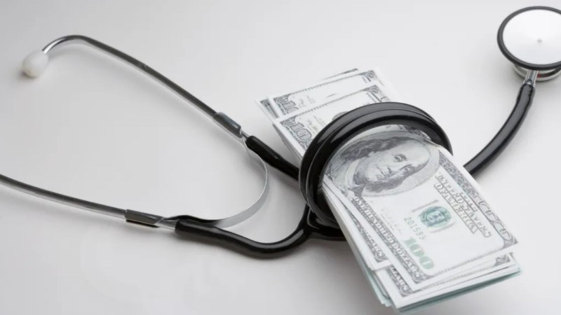 A blackstethoscope wrapped around a small stack of one-hundred-dollar bills.
