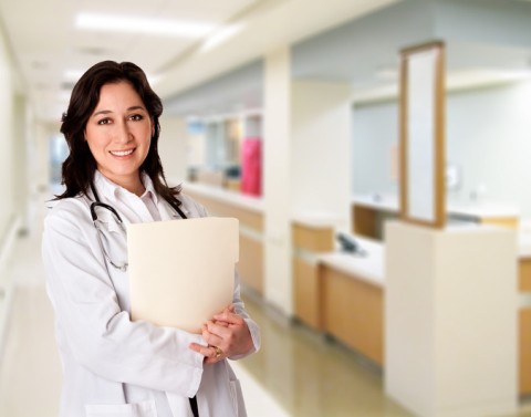 Woman medical professional with stethoscope around her neck and patient records in her arms in a medical hallway setting