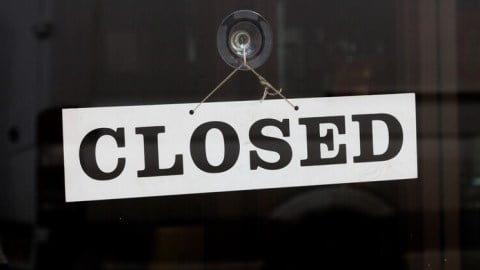 A white sign reading "closed" hanging on a glass door.