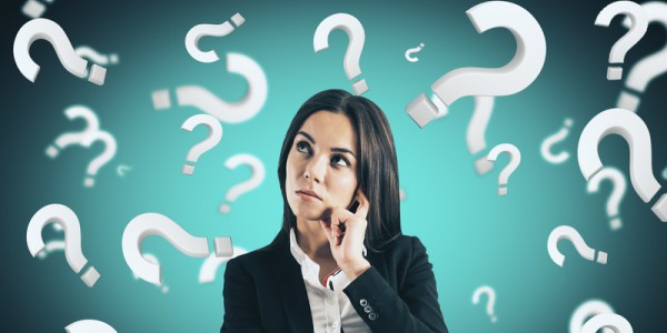 A businesswoman looking upward in concerned thought is surrounded by white 3D question marks