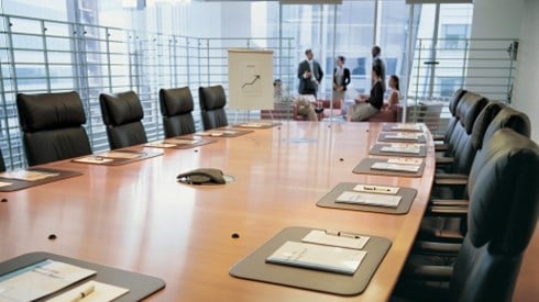A conference room table with a group of businesspeople having a meeting in the background
