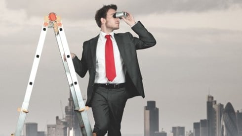 Businessman on an A-frame ladder looking through binoculars with a city skyline in the background